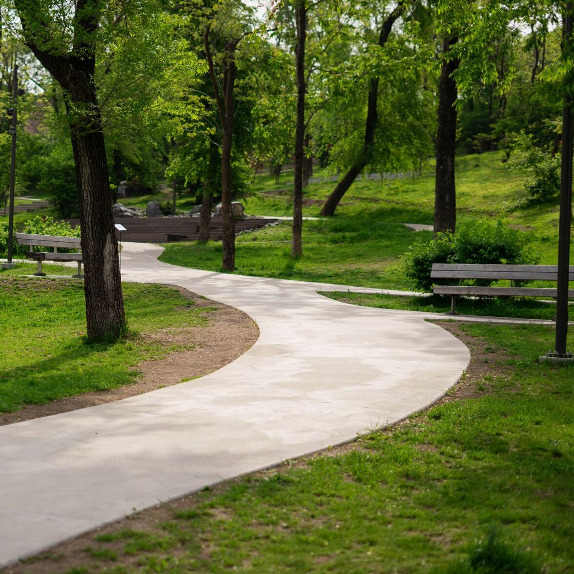 Scenic park-like setting with paved trail and park benches in wooded area 